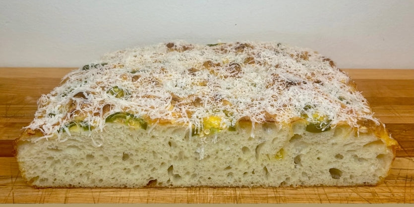 Loaf of bread with cheese and vegetables jalapeno on a wooden cutting board