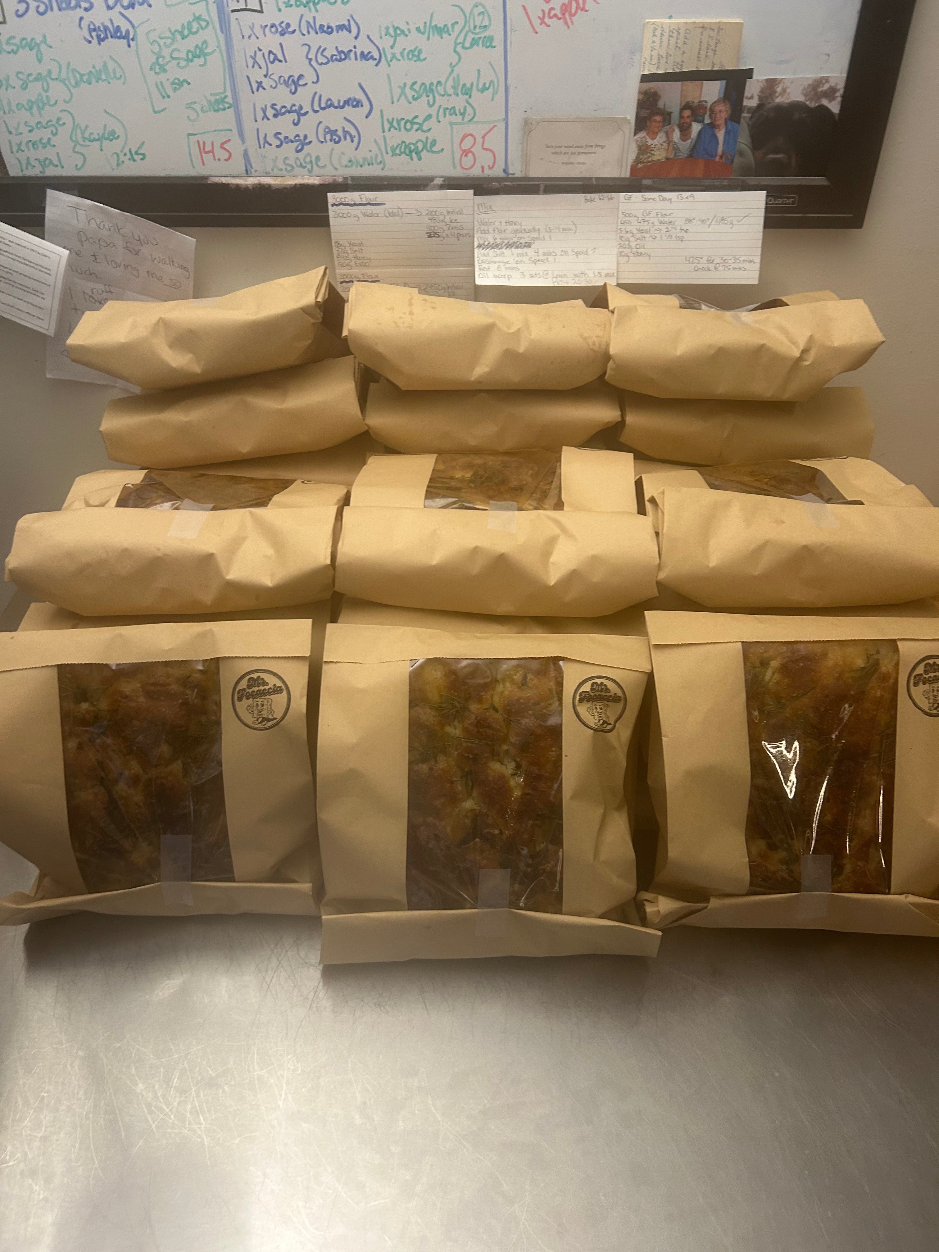 Stack of brown paper packages with windowed sections on a metallic surface, with a whiteboard in the background