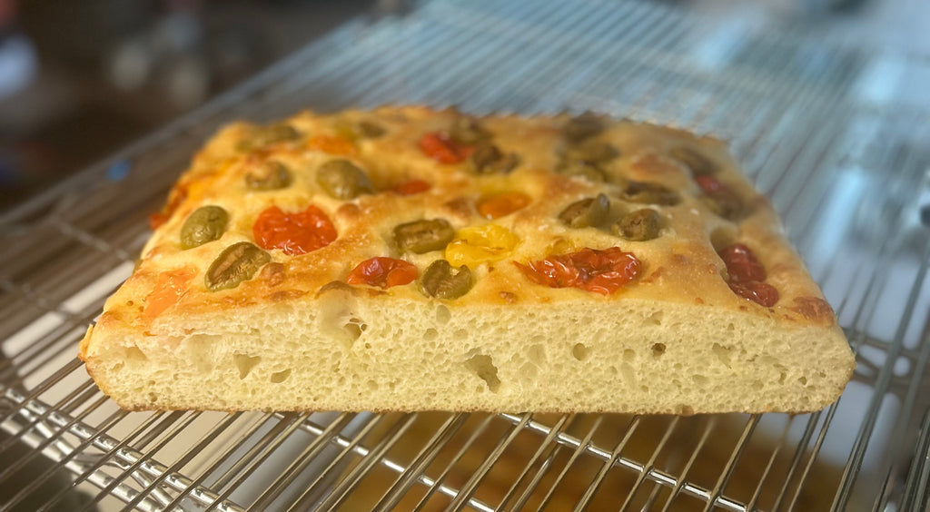 Rectangular focaccia bread with tomatoes and olives on a cooling rack.